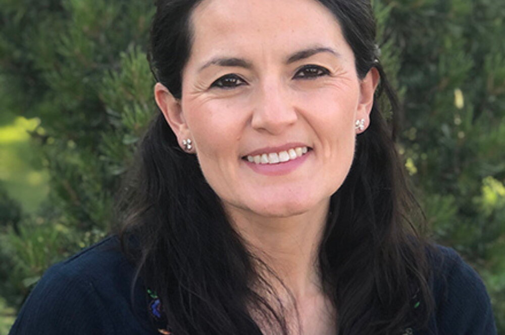 Paola Mera smiles for headshot outside with a background of trees.